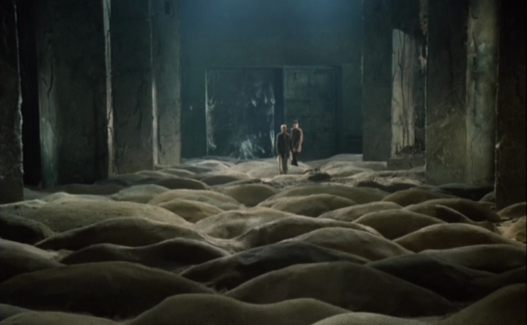 The Stalker and Professor stand in the room with rolling piles of sand.